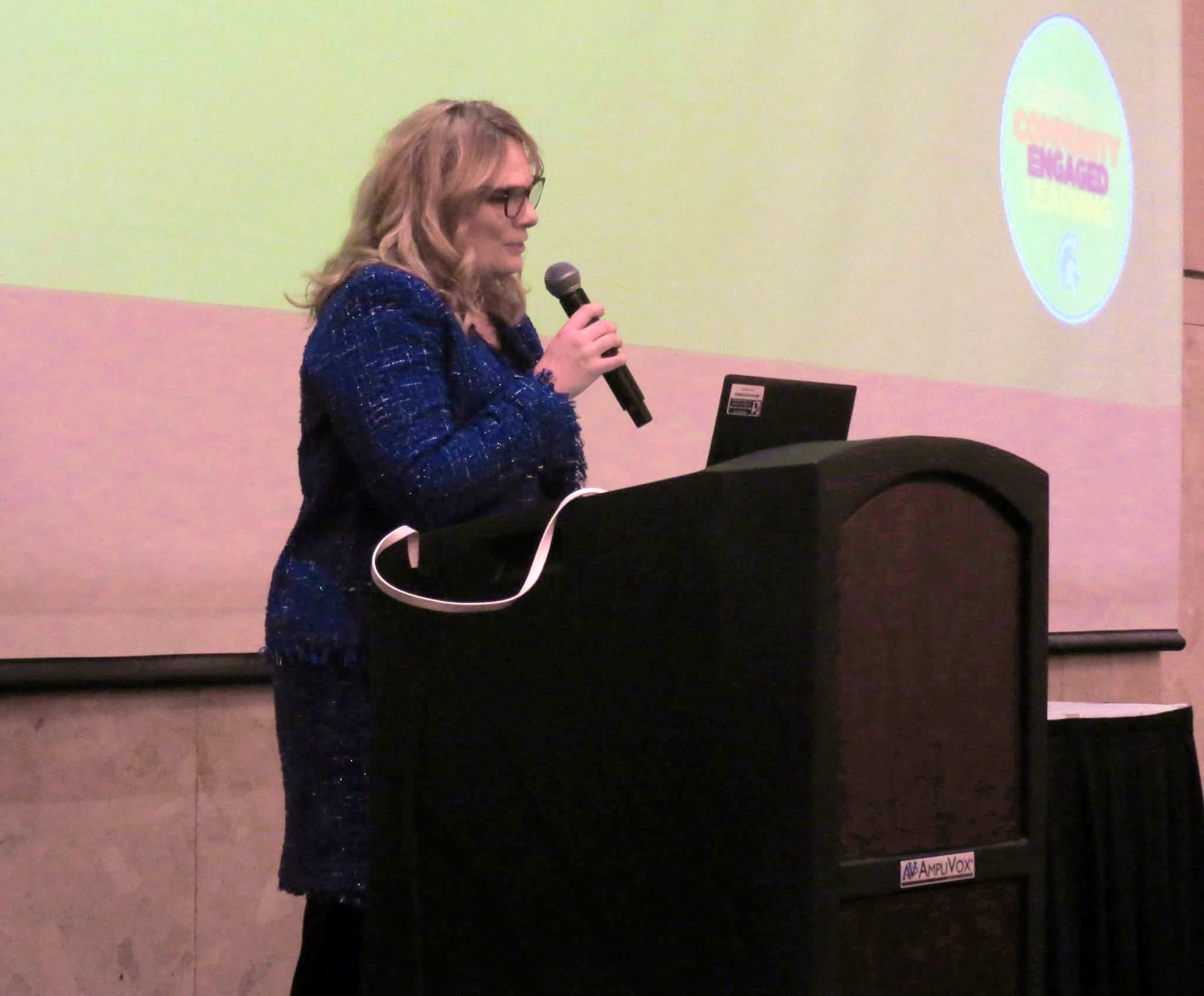 Renee Speaking at podium with screen presentation behind stage setup