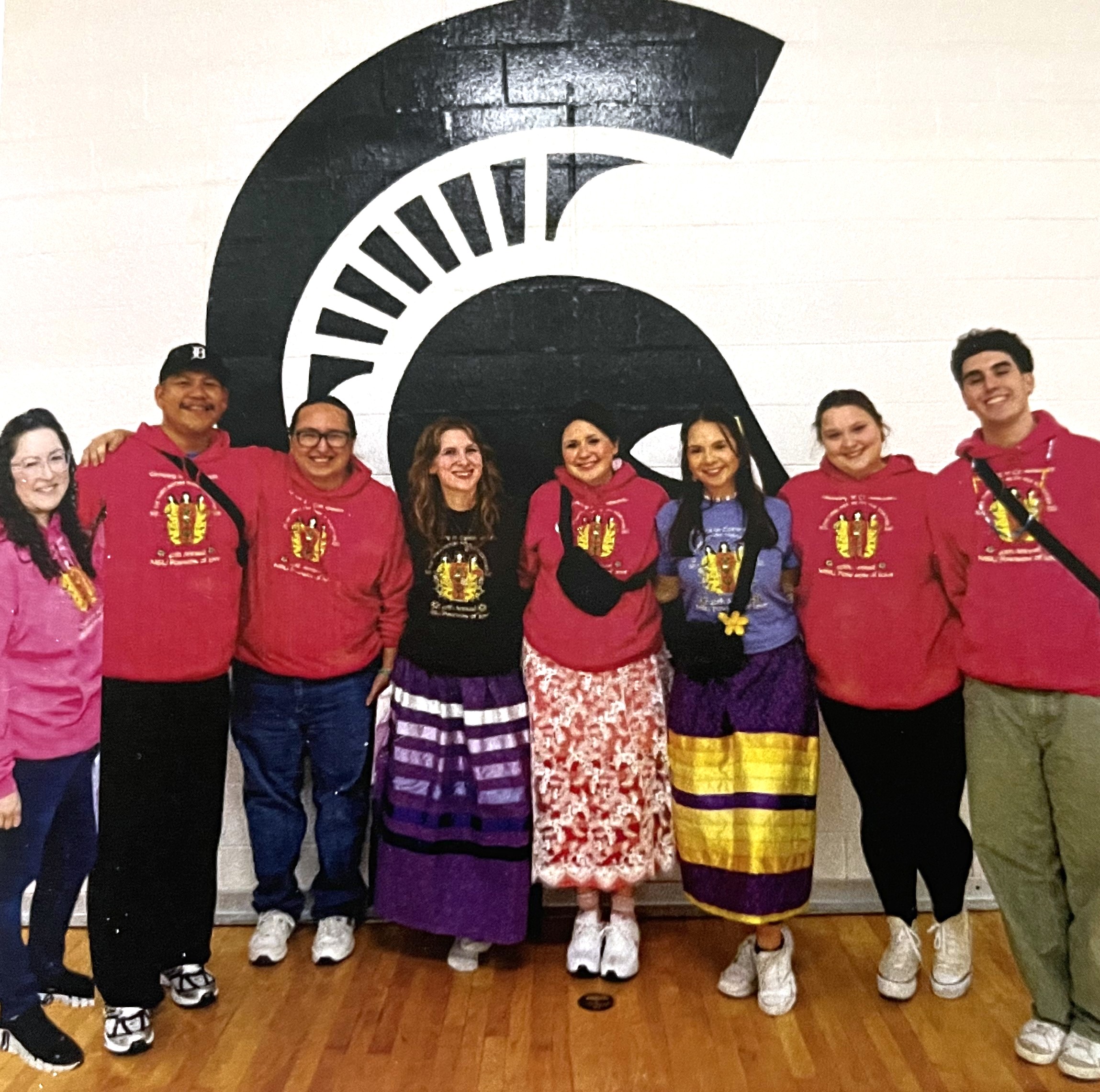 NAISO members and advisors pose in front of Spartan logo on a wall