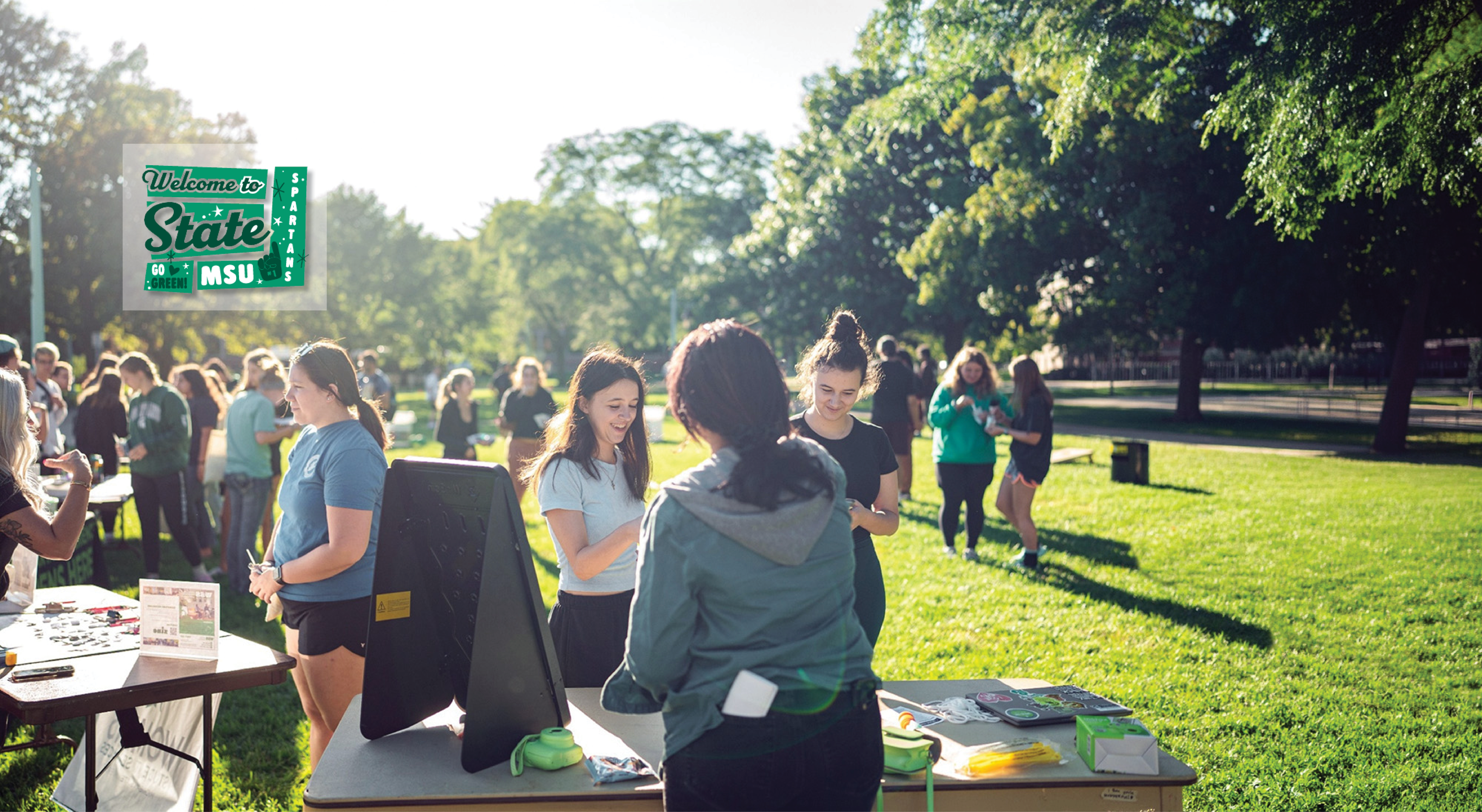 Students tabling with visitors on a sunny day in a field on campus