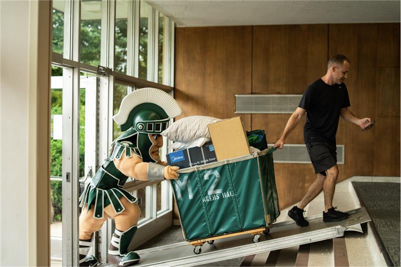 Sparty and student moving a bin up a ramp