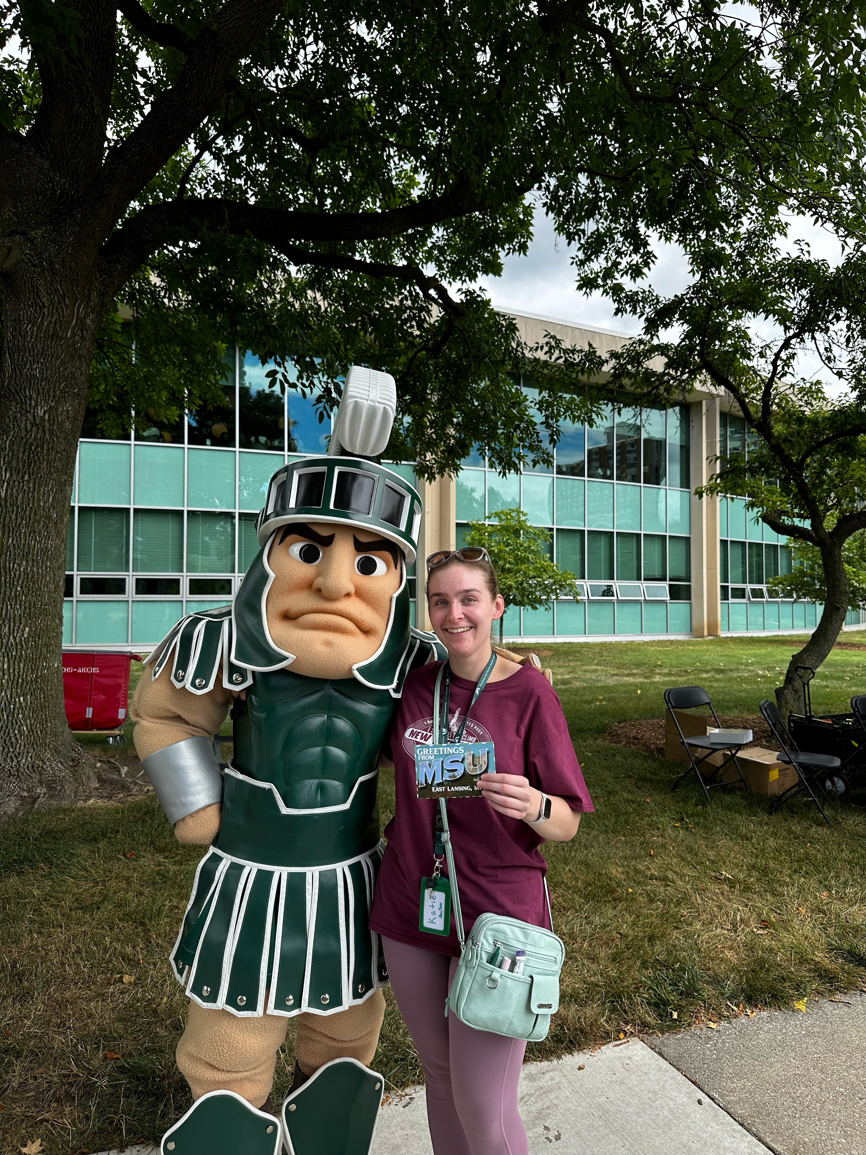 Student poses with Sparty outside a campus building