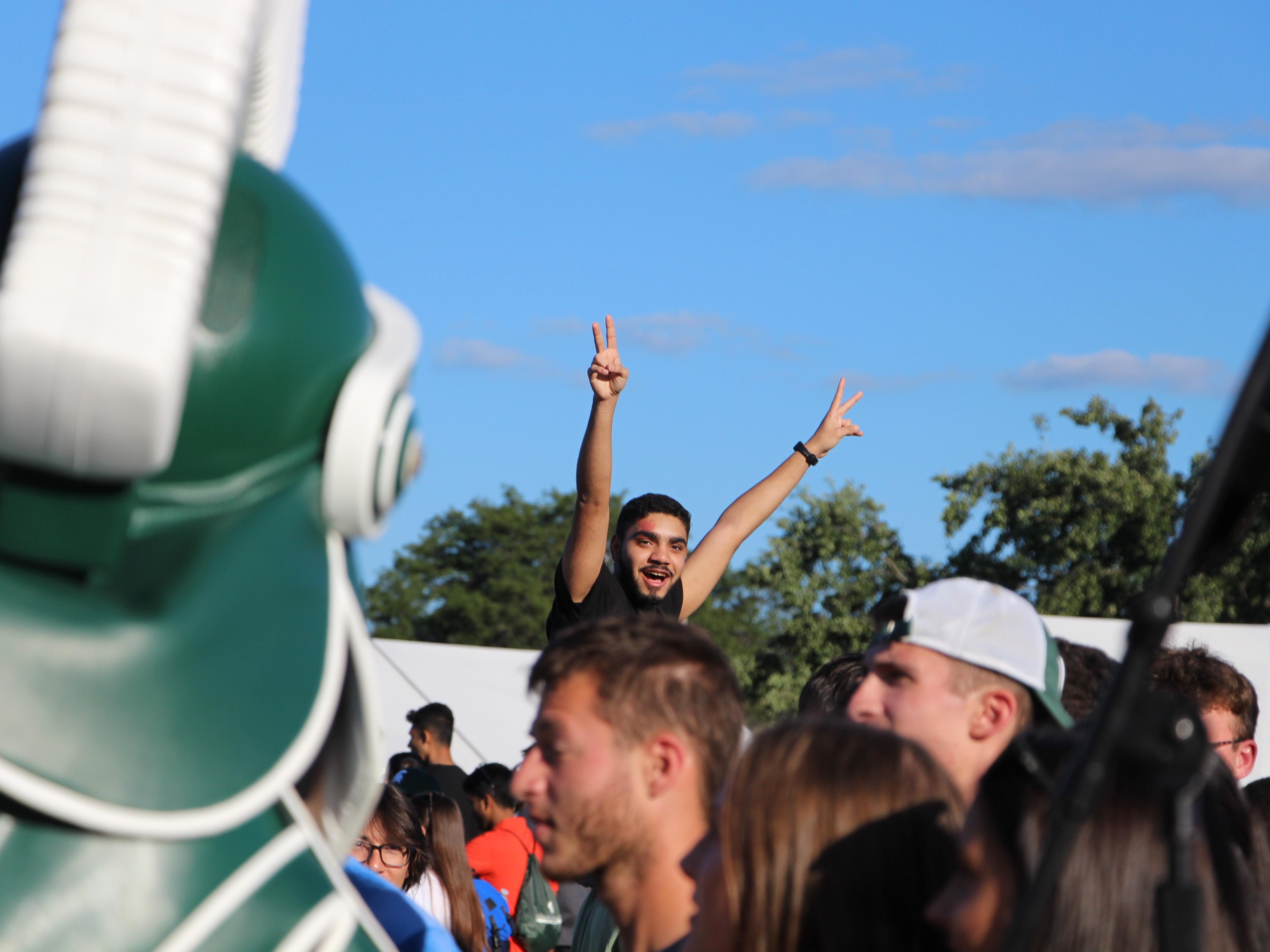 Student posing in a crowd with Sparty in foreground