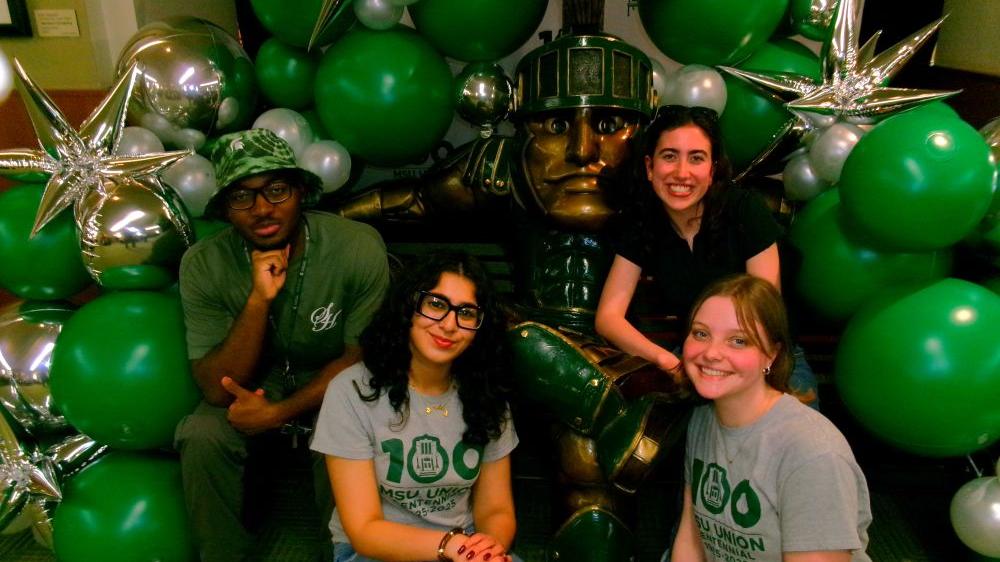 Students posing with Sparty statue, decorated in balloons
