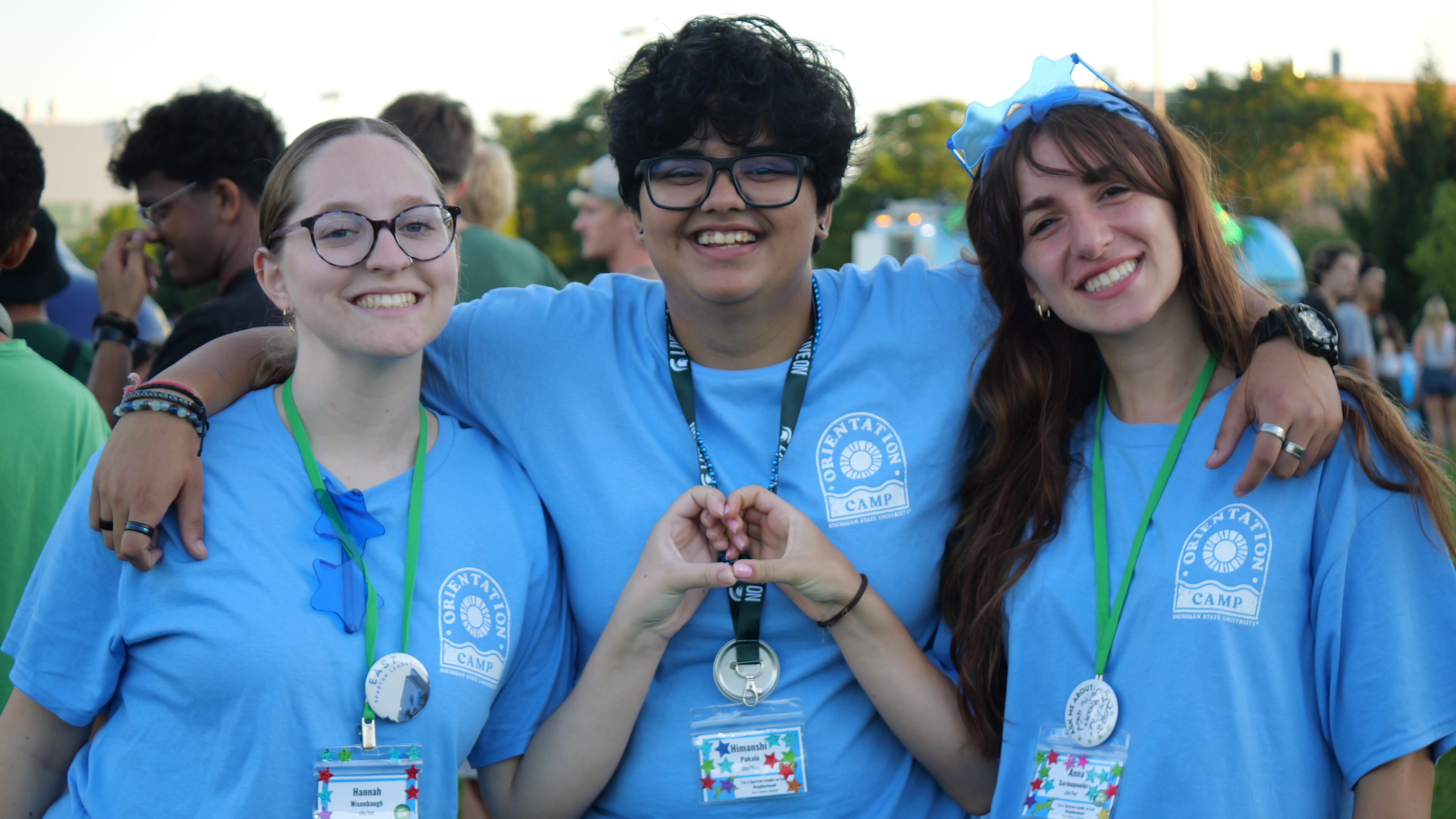 Three students wearing blue shirts smiling 