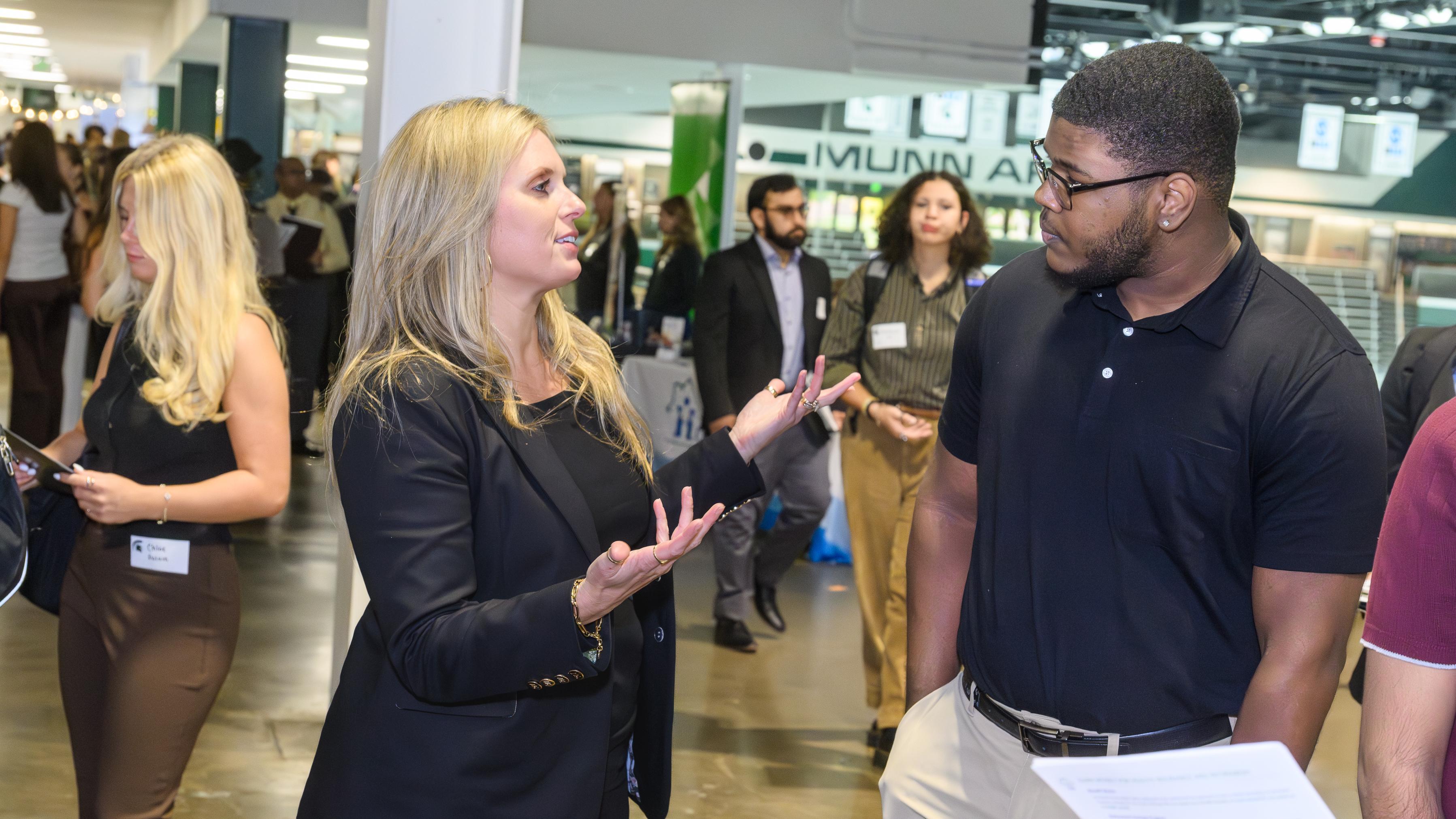 A student speaking to a company representative amongst others at a career fair