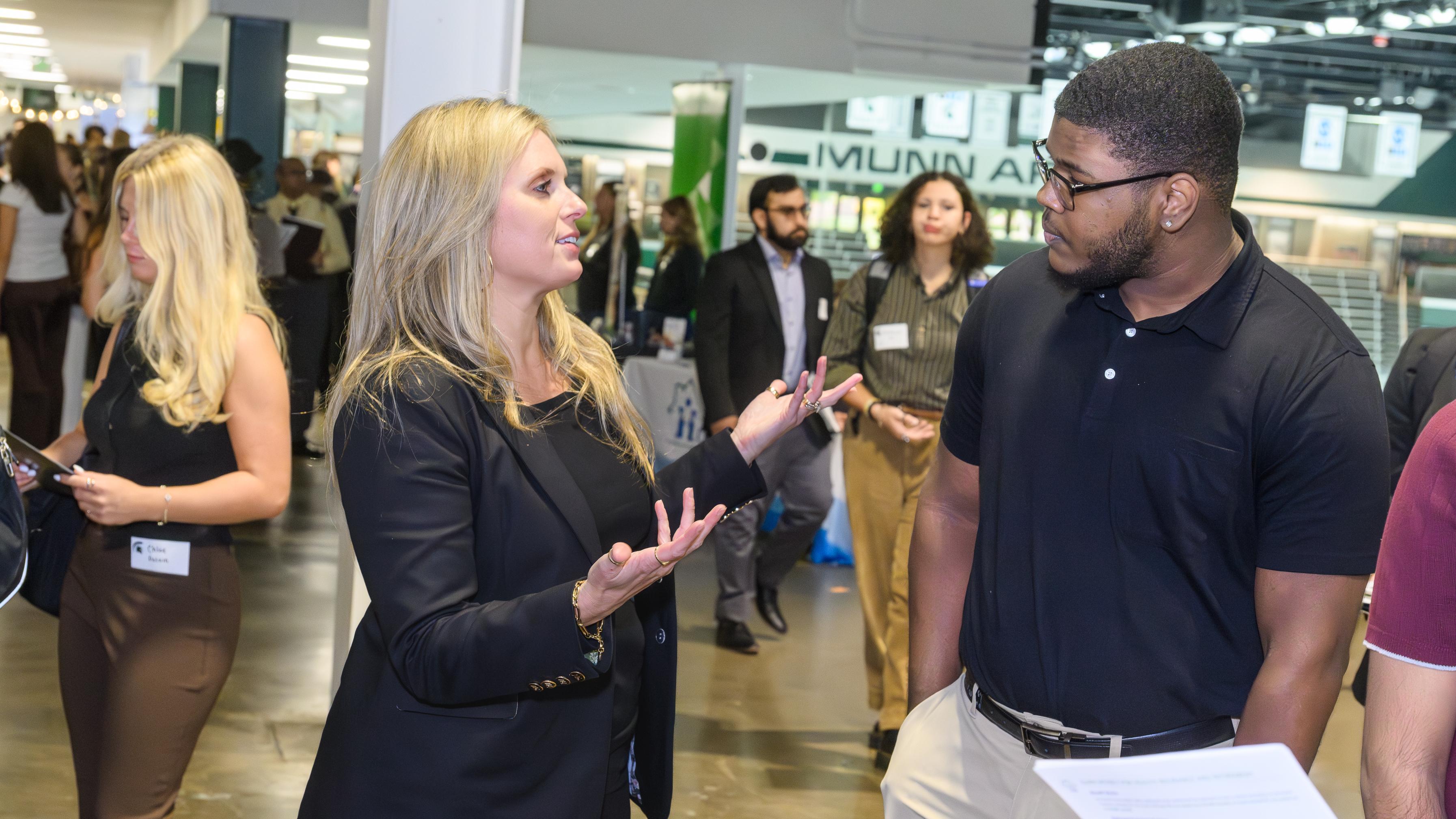 A student speaking to a company representative amongst others at a career fair