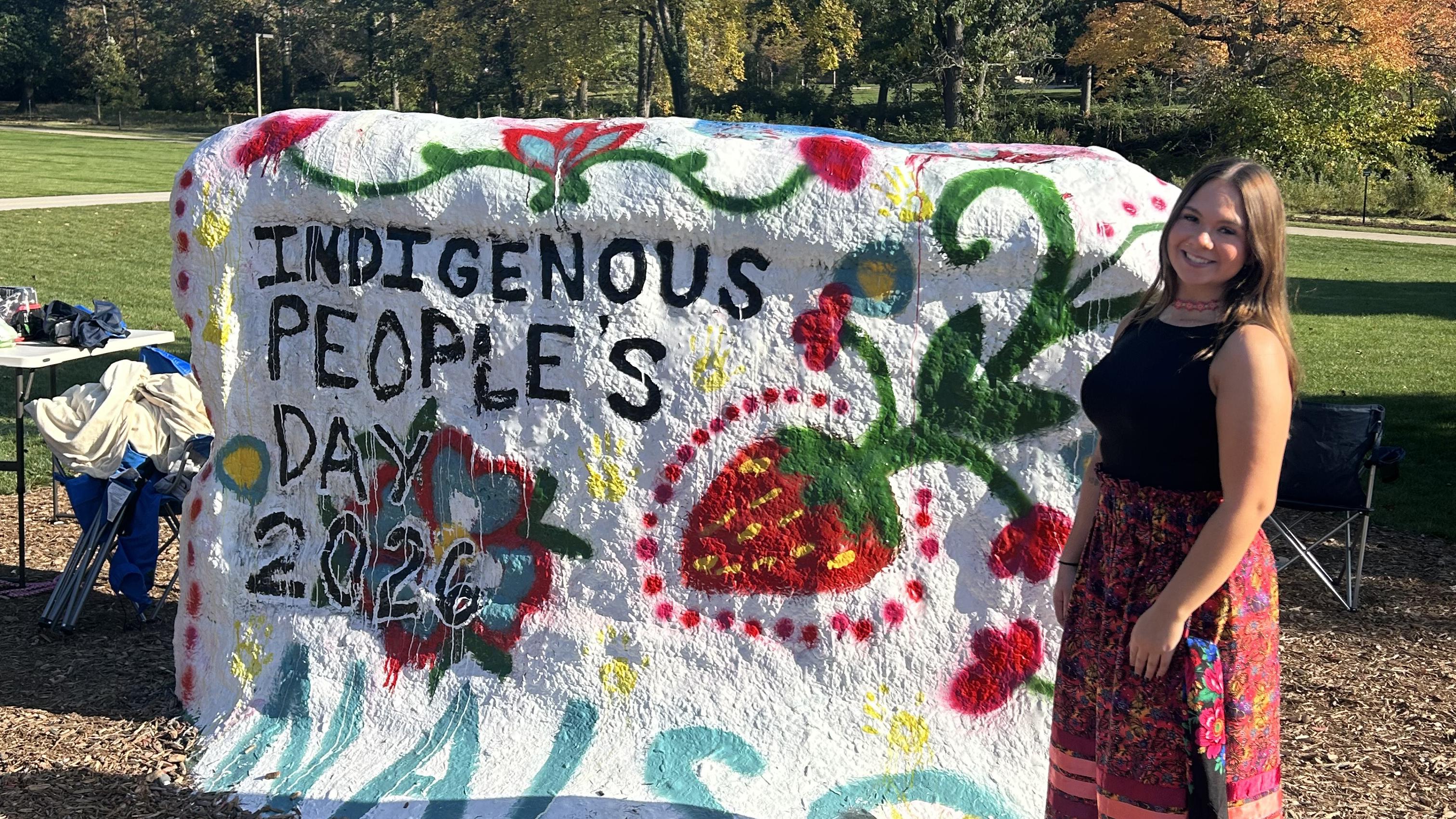 Student poses next to painted rock for Indigenous Peoples' Day