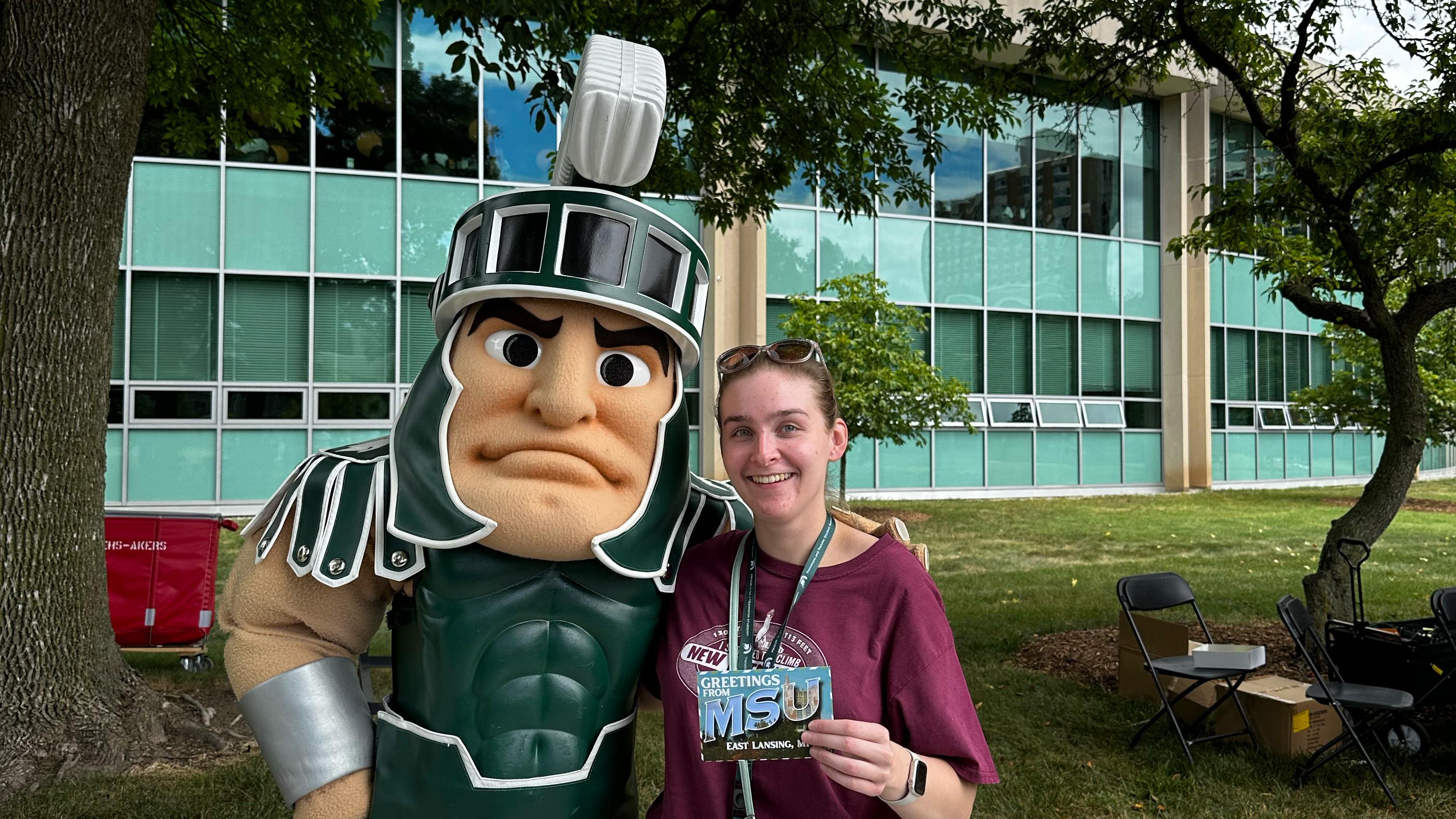 Student poses with Sparty outside a campus building